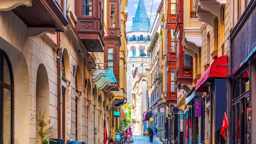 Galata Tower viewed from a narrow street in Istanbul, surrounded by historic buildings.