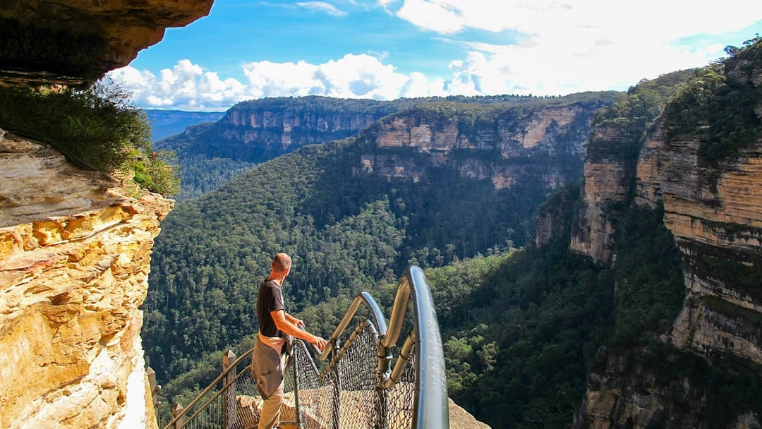 Person standing on lookout at Blue Mountains, Australia, overlooking forested cliffs.