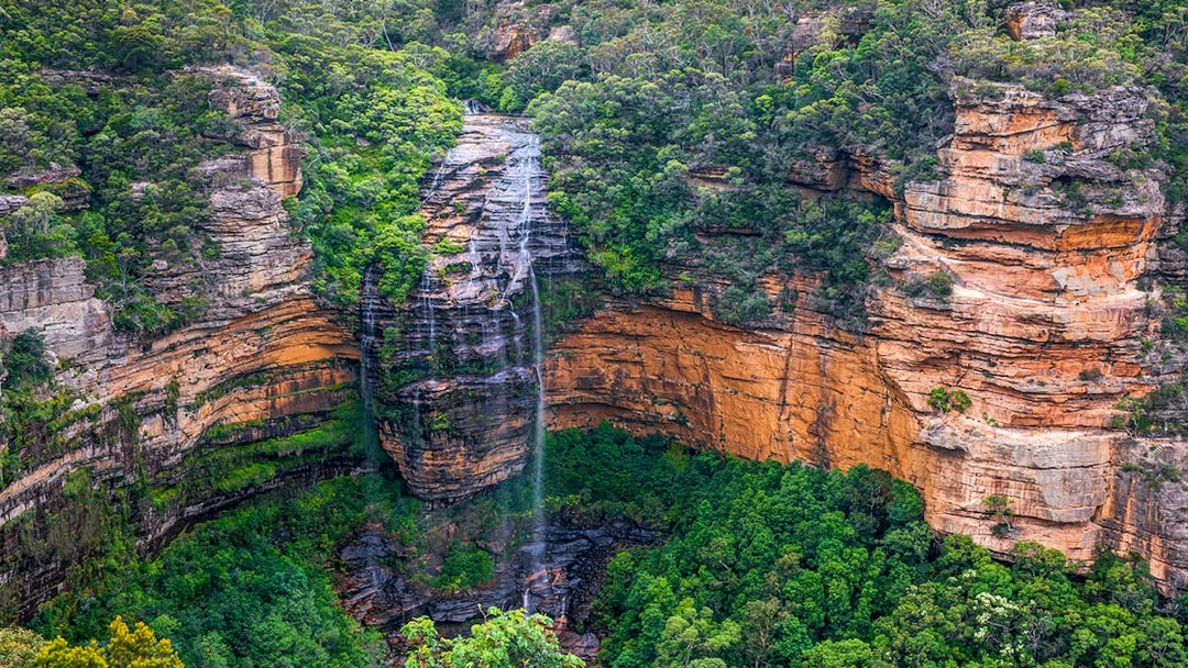 Wentworth Falls cascading over cliffs in Blue Mountains, surrounded by lush greenery.