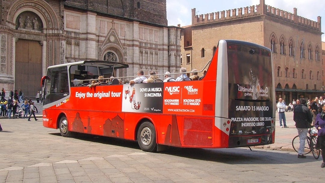 Red double-decker bus in Bologna city center, part of hop-on hop-off tour with food tasting vouchers.