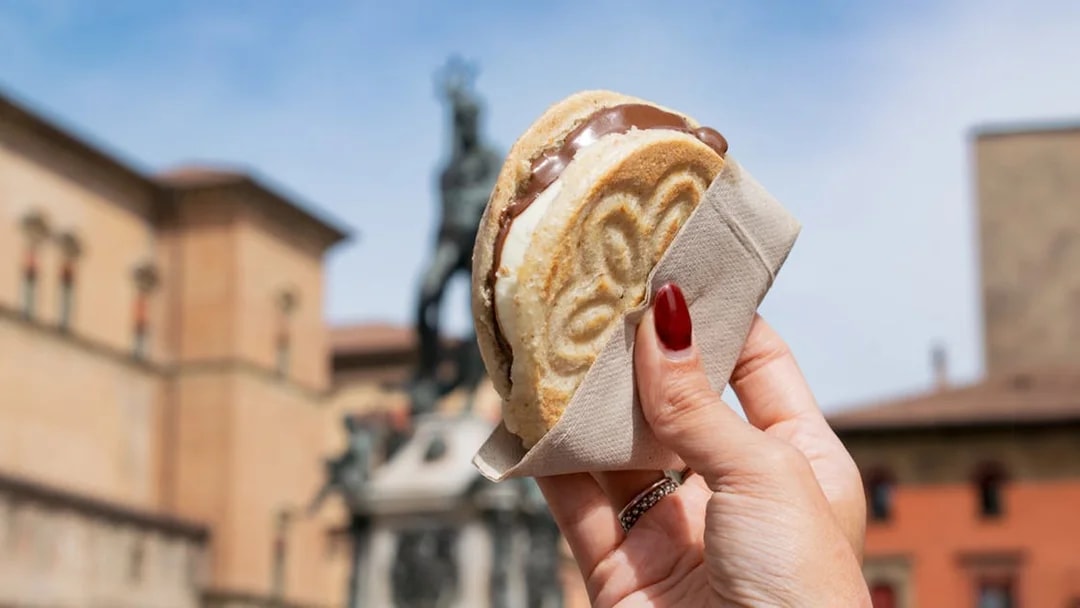 Hand holding an ice cream sandwich in front of a historic building in Bologna.