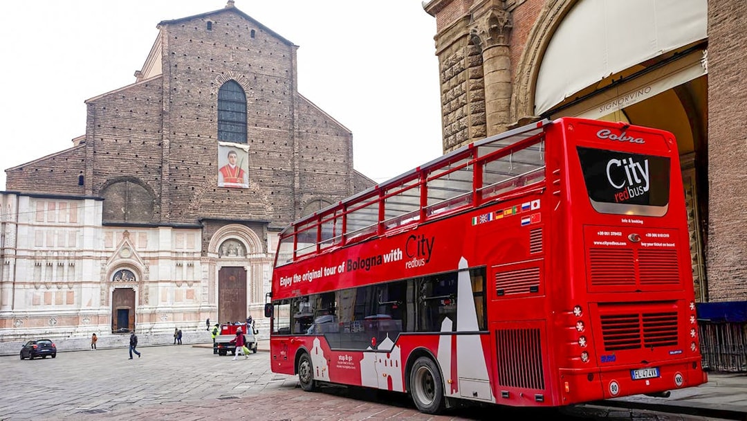Red City tour bus in Bologna near historic church, part of hop-on hop-off tour with food tasting vouchers.