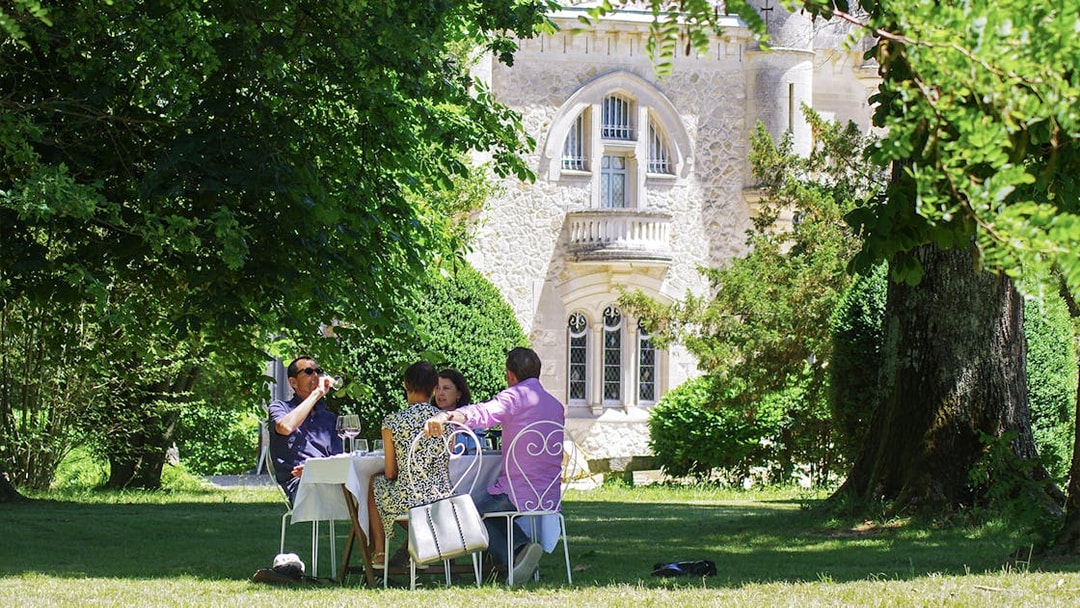 Group enjoying wine at a table in a garden near a historic building in Saint-Emilion.