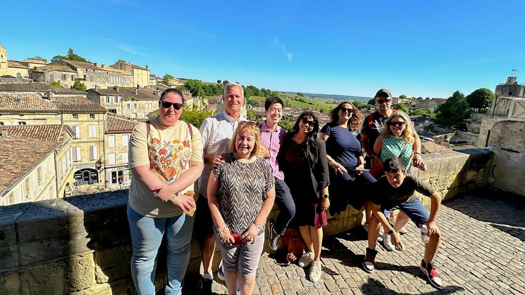 Tour group enjoying a sunny day in Saint-Emilion village with historic buildings in the background.