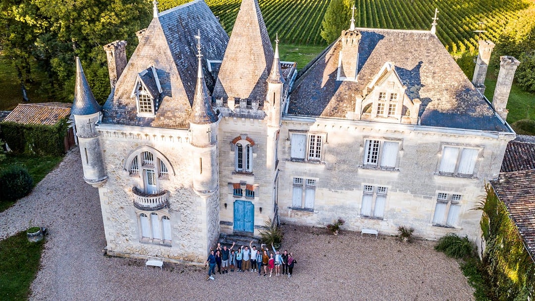 Saint-Emilion chateau with group of tourists in courtyard, surrounded by vineyards.