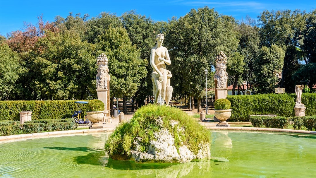 Statue and fountain in Borghese Gardens, Rome, surrounded by greenery.