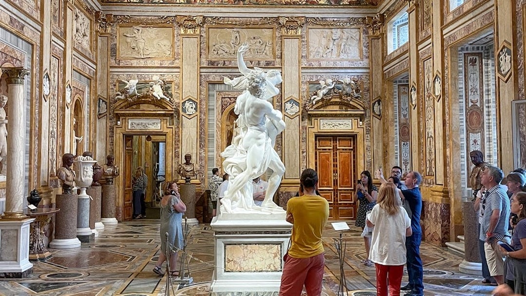 Sculpture of The Rape of Proserpina in Borghese Gallery, Rome, surrounded by visitors.
