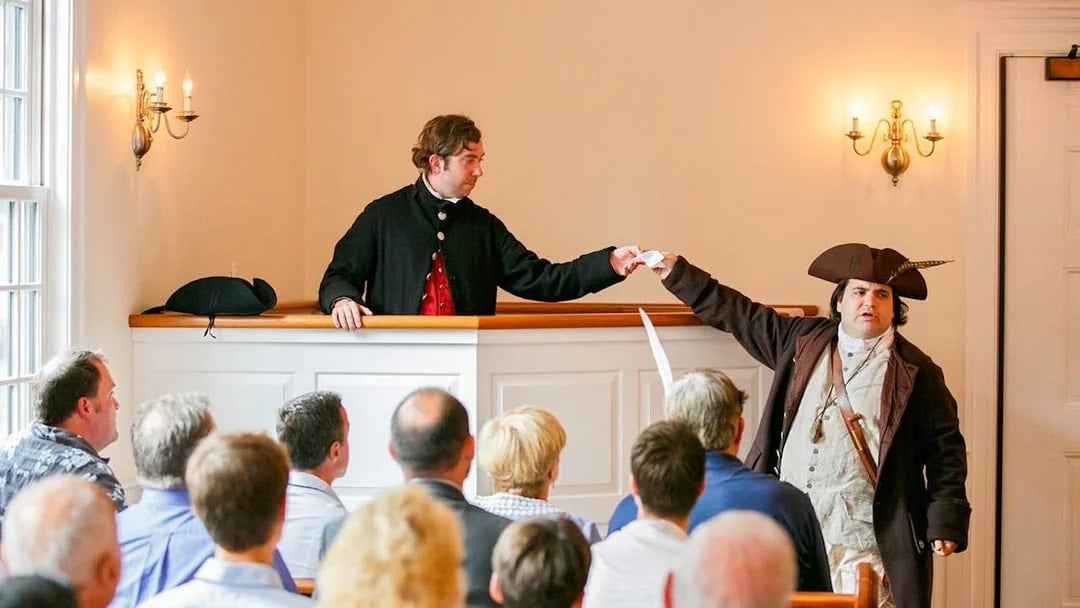Reenactment of Boston Tea Party debate with actors in period costumes inside a historic room.