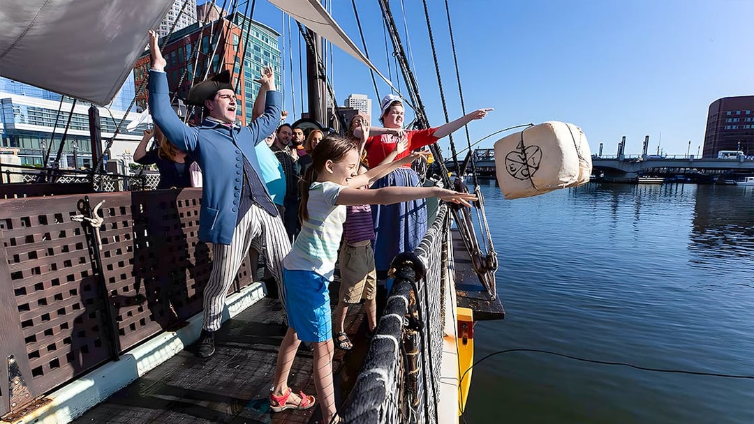 Tourists reenact Boston Tea Party by throwing tea chest from ship into harbor.