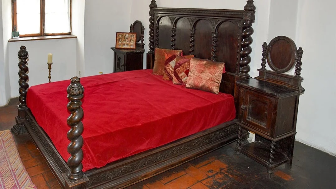 Wooden medieval bed in Bran Castle bedroom with red bedding.