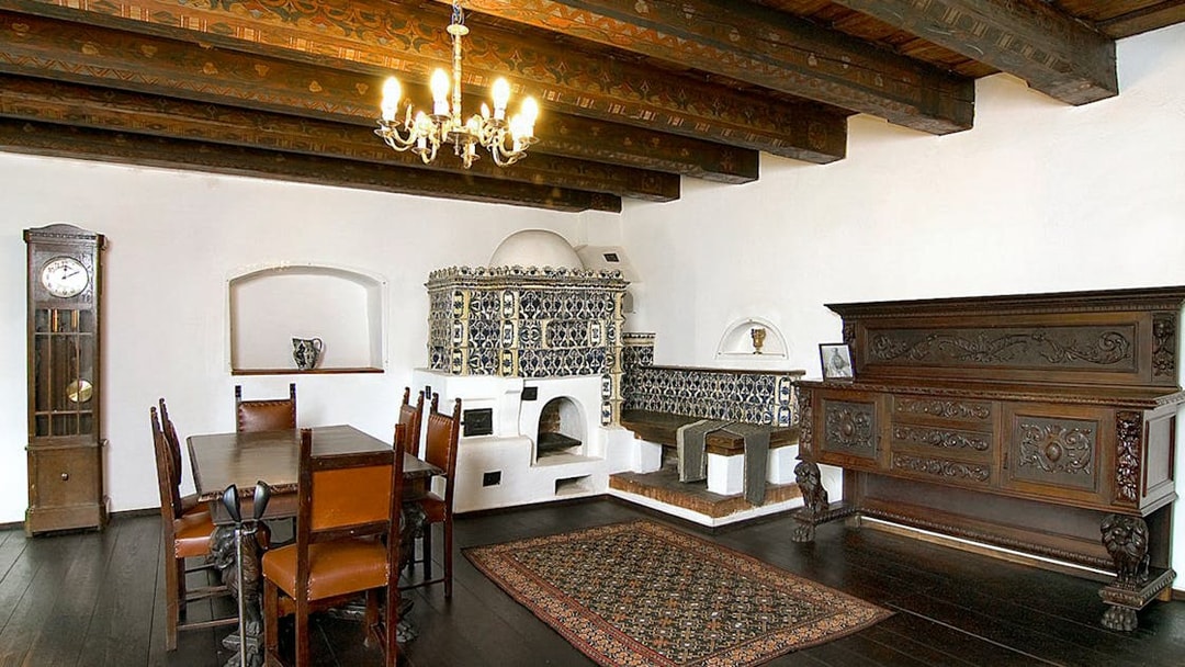 Bran Castle interior with ornate stove, wooden dining table, and antique furniture.