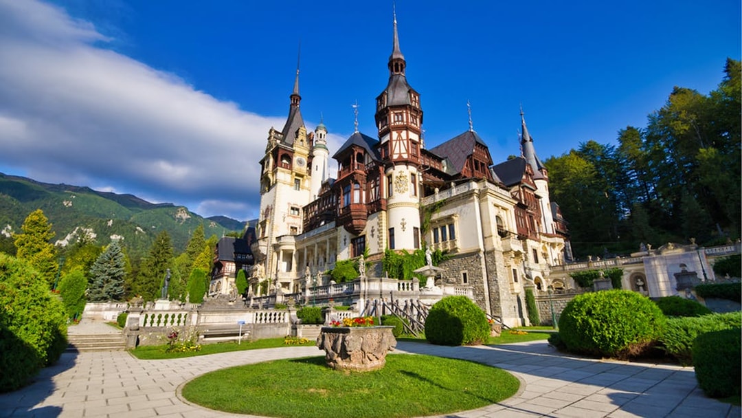 Peles Castle in Sinaia, Romania, with gardens and mountain backdrop.