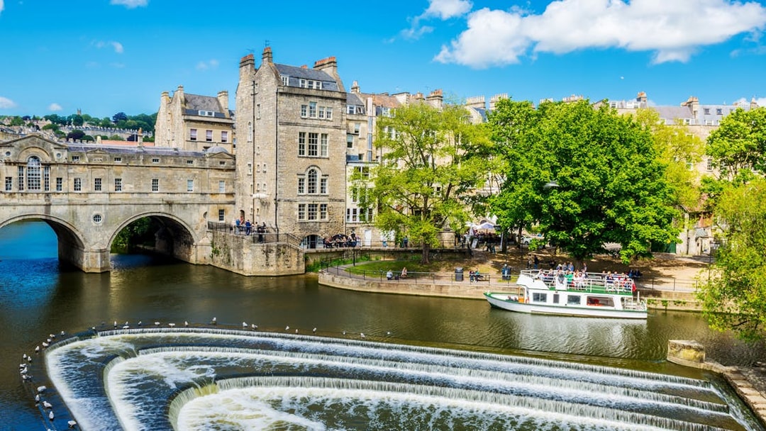 Historic Bath city street with tour group near Pulteney Bridge, live music performance nearby.