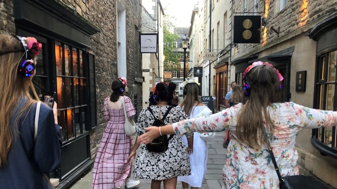 Tour group in period costumes with headphones walking through Bath's historic streets.