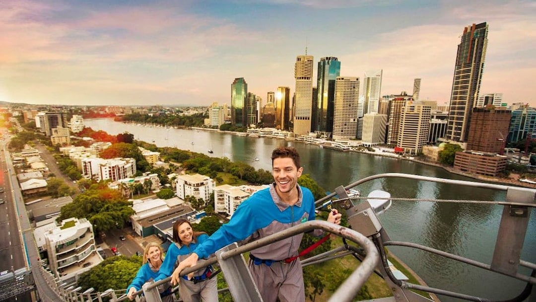 Climbers ascending Brisbane's Story Bridge with city skyline and river view.