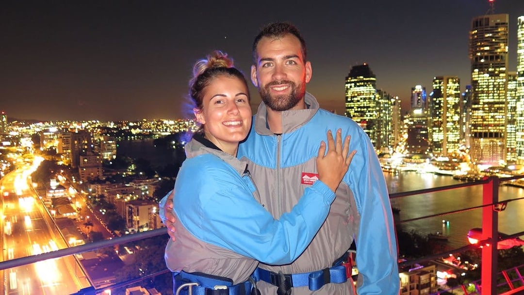 Couple on Brisbane Story Bridge during twilight climb with city lights in background.