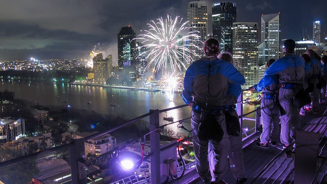 Climbers on Brisbane Story Bridge watching fireworks over the city at twilight.