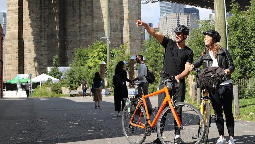 Couple with bikes near Brooklyn Bridge, New York City, enjoying a guided tour.