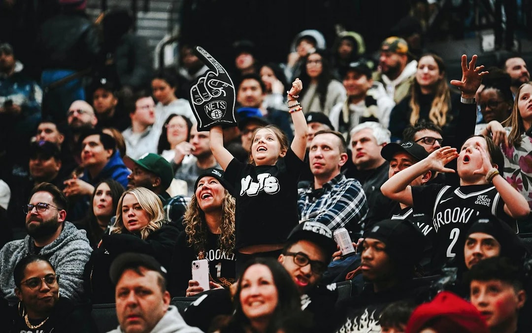 Crowd cheering at a Brooklyn Nets game, child holding foam finger.