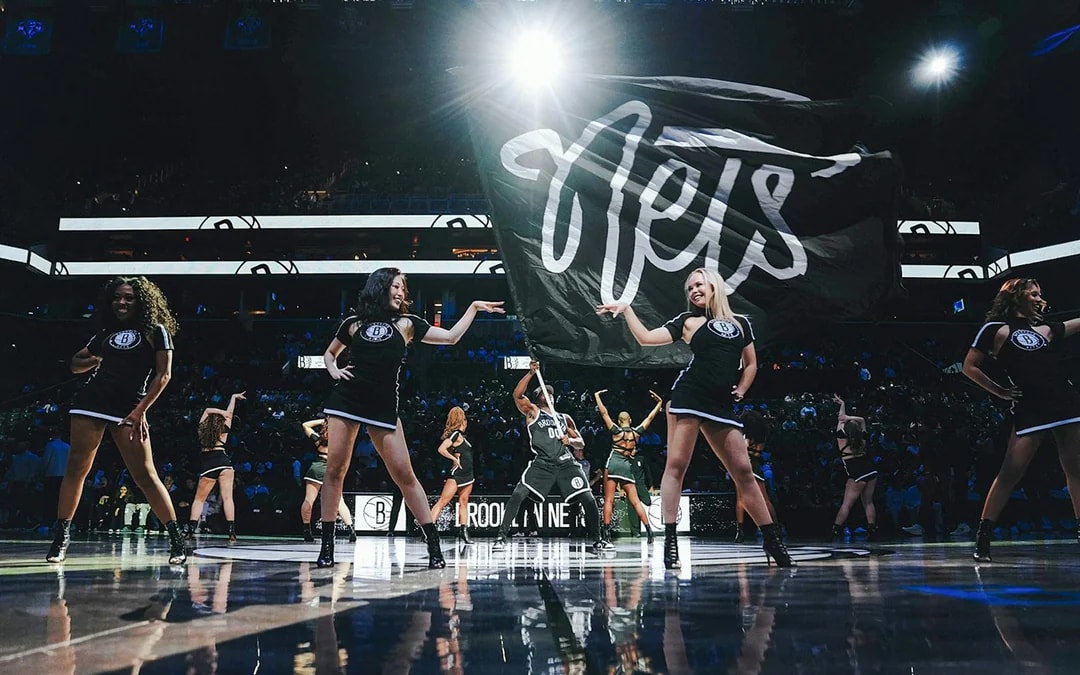 Brooklyn Nets cheerleaders performing on court with large Nets flag.