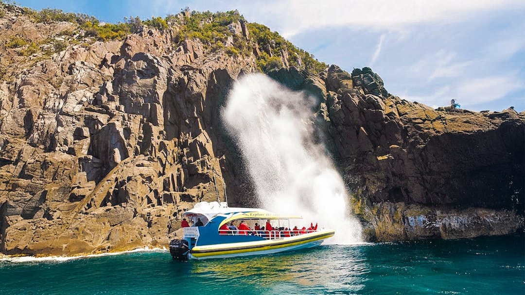 Cruise boat near rocky cliffs and waterfall on Bruny Island Wilderness Cruise.