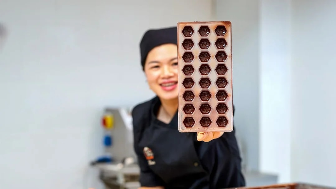Chocolatier holding a tray of chocolate molds at Choco Story Brussels.