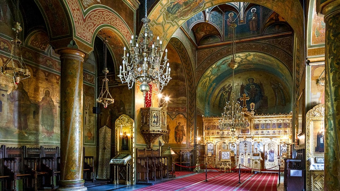 Interior of a richly decorated church with ornate chandeliers and religious frescoes, part of the Dracula's Castle day trip from Bucharest.