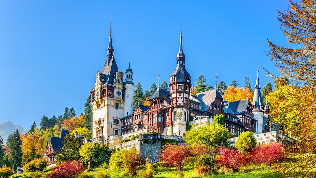 Peles Castle exterior in Romania surrounded by autumn trees.