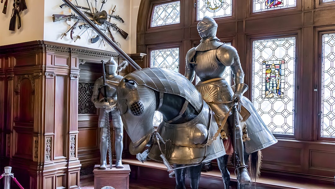 Knight armor display inside Peles Castle with stained glass windows.