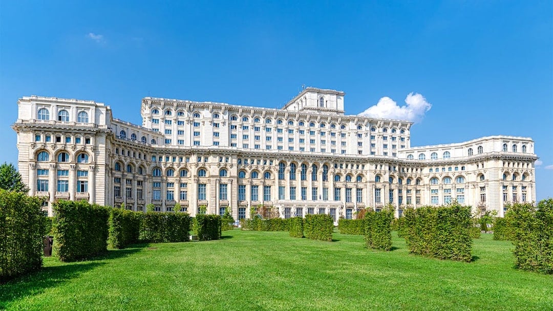 Palace of the Parliament in Bucharest with manicured gardens in the foreground.