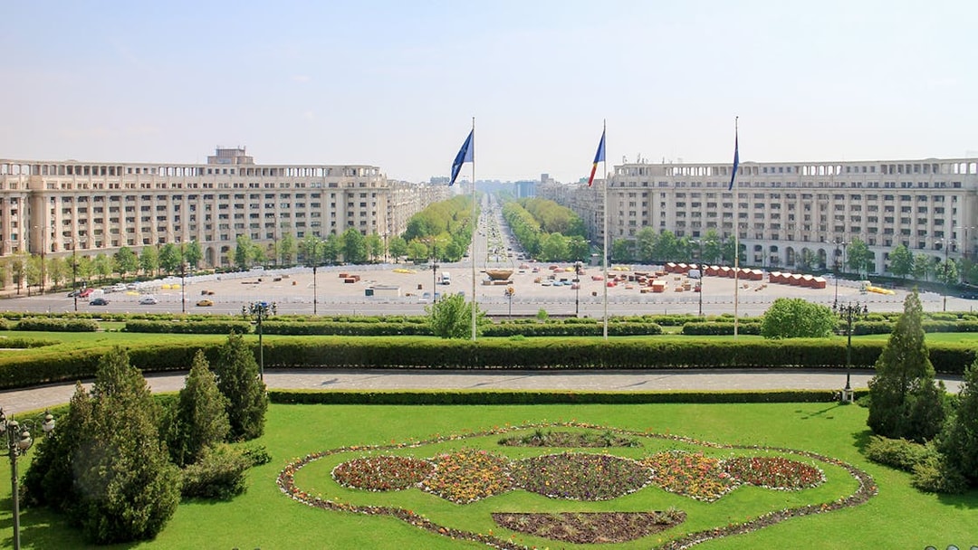 Unirii Boulevard view from Palace of the Parliament, Bucharest, with symmetrical gardens and flags.