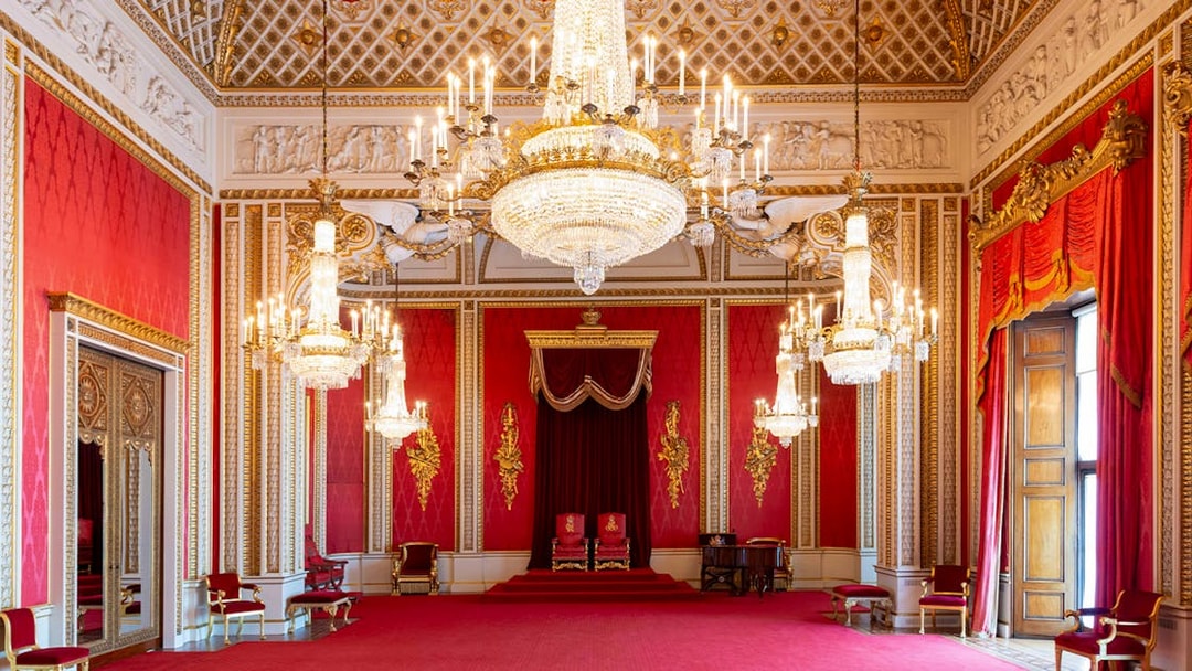 Throne Room at Buckingham Palace with ornate chandeliers and red decor.