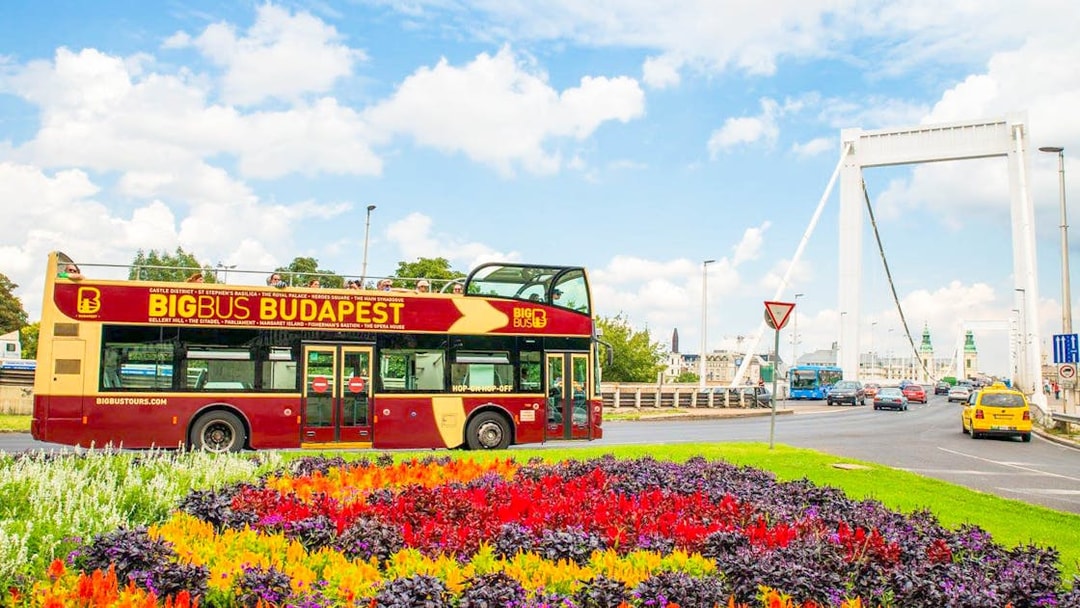 Budapest Big Bus passing by colorful flower beds near Elizabeth Bridge.