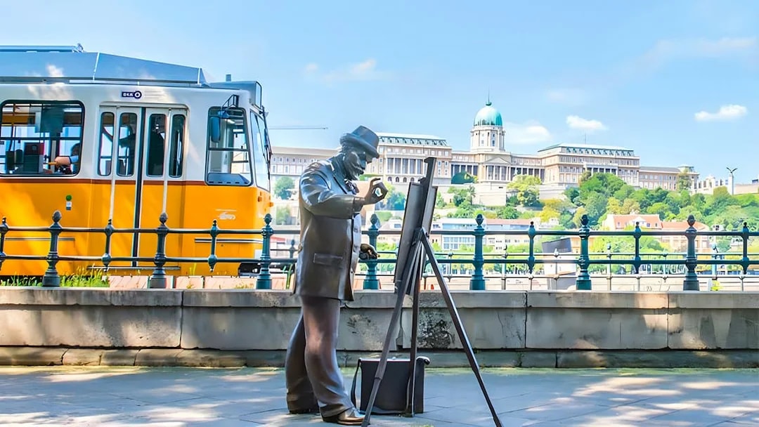 Tram passing by a statue of a painter with Buda Castle in the background, Budapest.