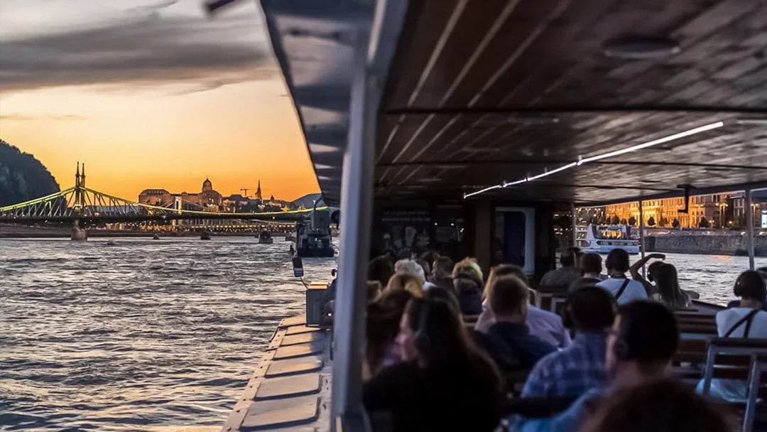 Danube River cruise at sunset with passengers and view of Liberty Bridge, Budapest.