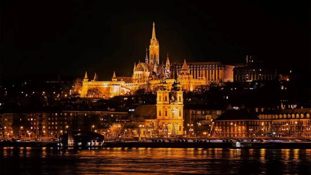 Matthias Church illuminated at night from a Danube River cruise in Budapest.