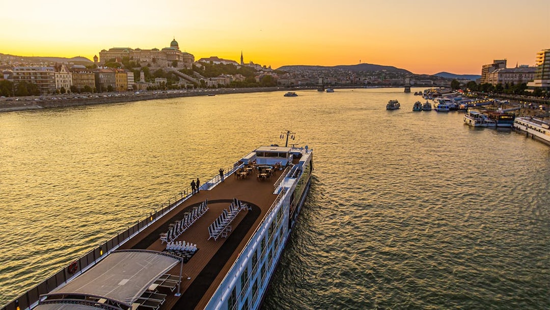 Cruise ship on the Danube River at sunset with Budapest skyline in the background.