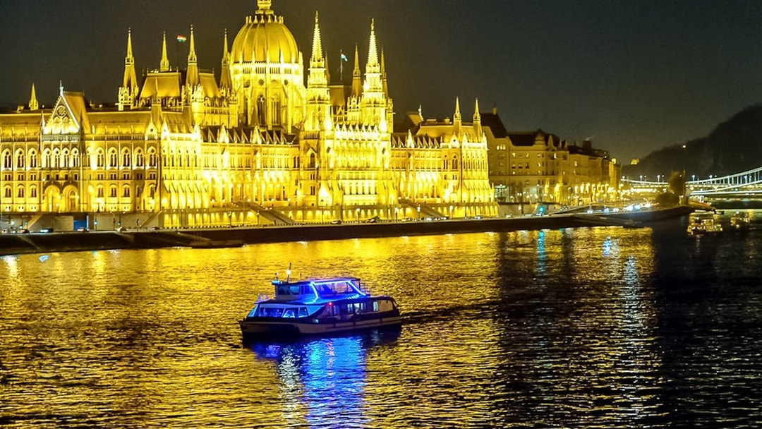 Cruise boat on Danube River with Budapest Parliament illuminated at night.