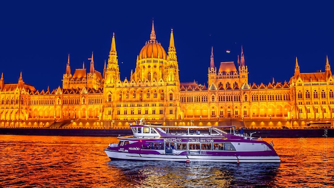 Budapest Parliament lit up at night with a cruise boat on the Danube River.