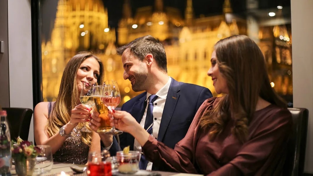 Guests toasting on a Budapest dinner cruise with a piano battle show in the background.