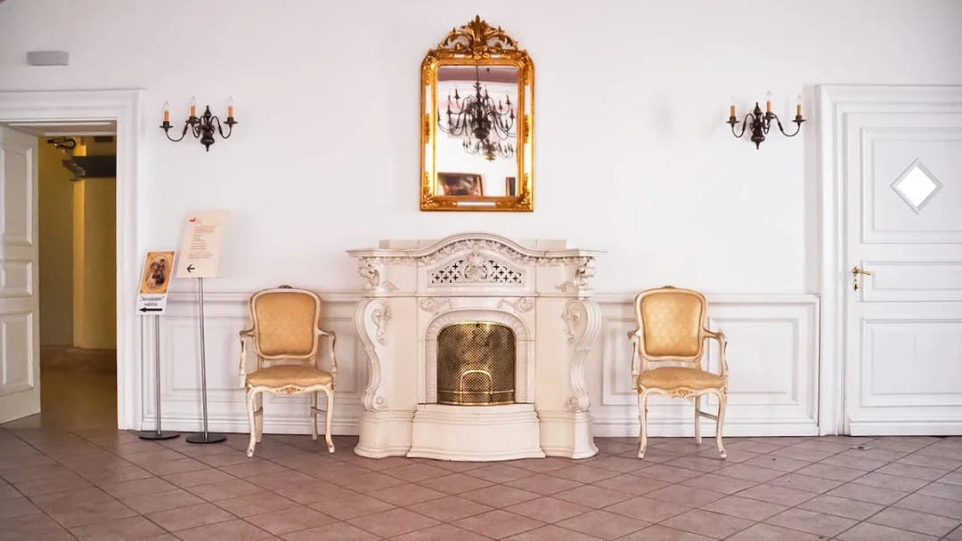 Elegant interior of Gödöllő Palace with ornate fireplace and chairs, Budapest tour.