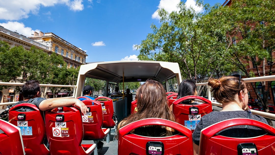 Open-top bus tour with passengers in a city setting, surrounded by trees and historic buildings.