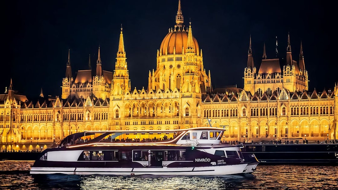 Cruise boat on Danube River at night with Budapest Parliament illuminated in background.