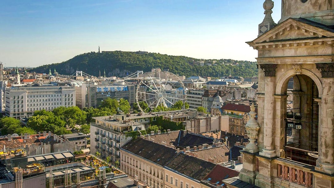 View of Budapest cityscape from St. Stephen's Basilica, featuring a Ferris wheel and Gellért Hill.
