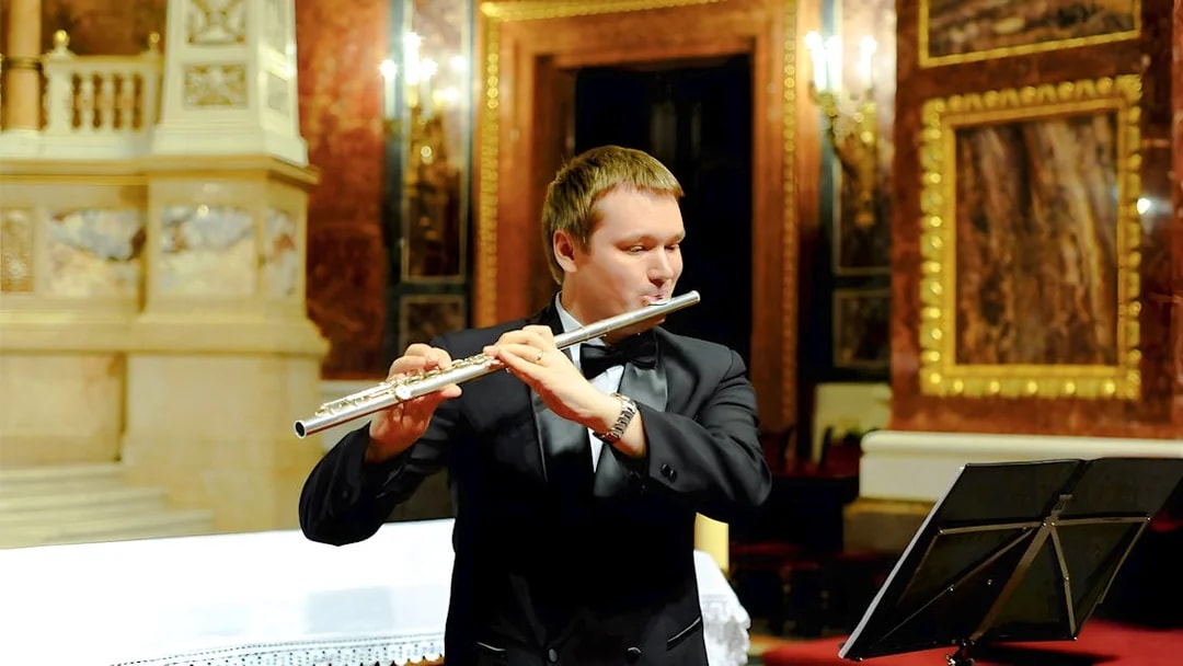Man in black suit playing silver flute at St. Stephen's Basilica concert.