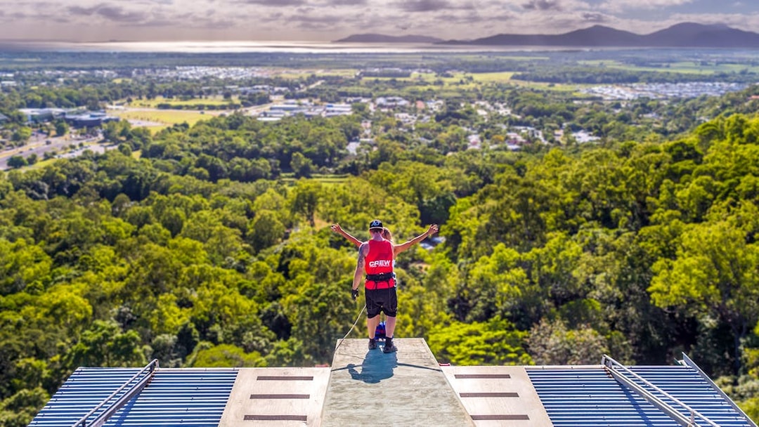 Bungy jumper on platform overlooking Cairns landscape, preparing to jump.