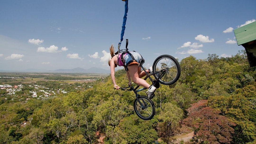 Person bungy jumping with a bicycle over lush landscape in Cairns, Australia.