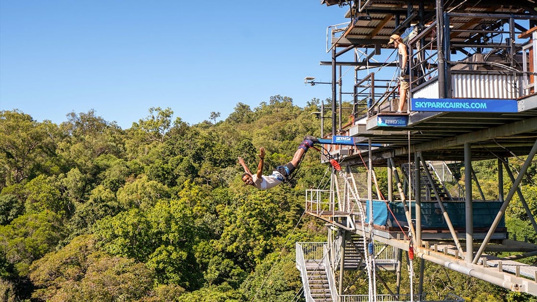 Person bungy jumping from platform at Skypark Cairns, surrounded by lush greenery.