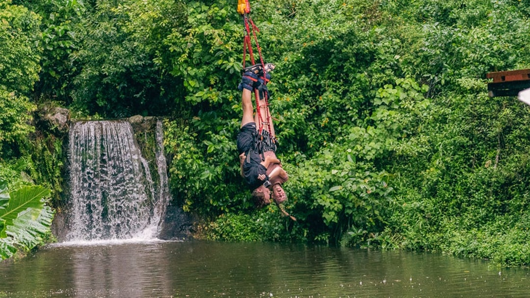 Bungy jumper over lush greenery and waterfall in Cairns, Australia.