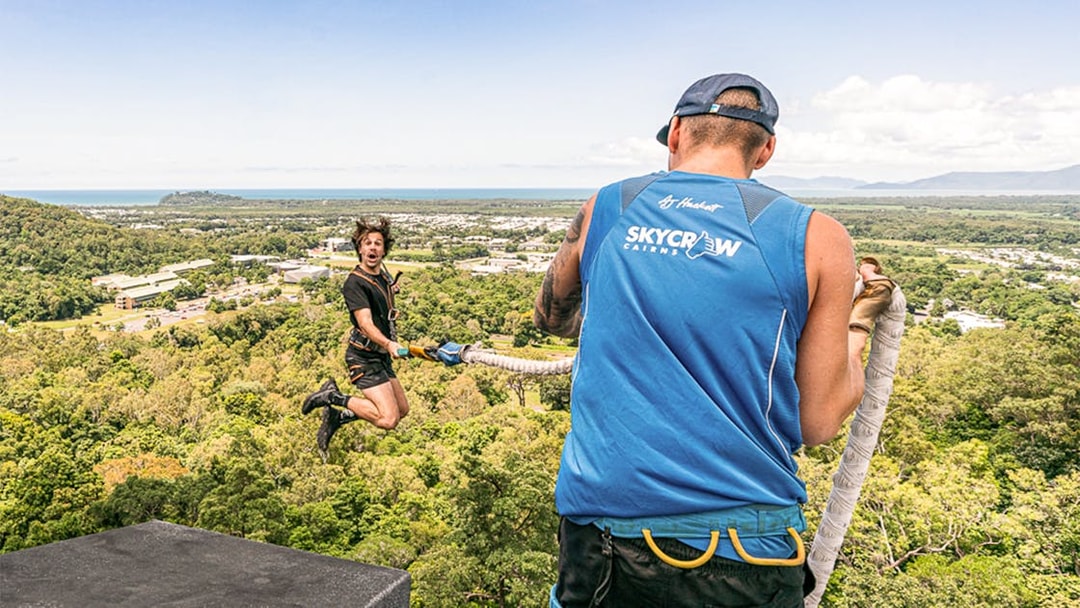 Bungy jumper mid-air with instructor overlooking Cairns landscape.